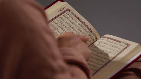 close up of muslim woman sitting on sofa at home reading or studying the quran 1