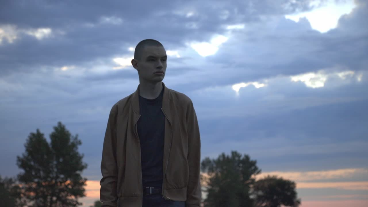 Young Man Walking Towards The Camera With Sunset Sky On The Background. - medium shot