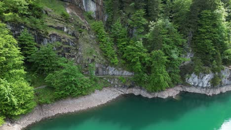 Beautiful-hilly-road-adorned-by-Alpine-forest-and-turquoise-lake-water