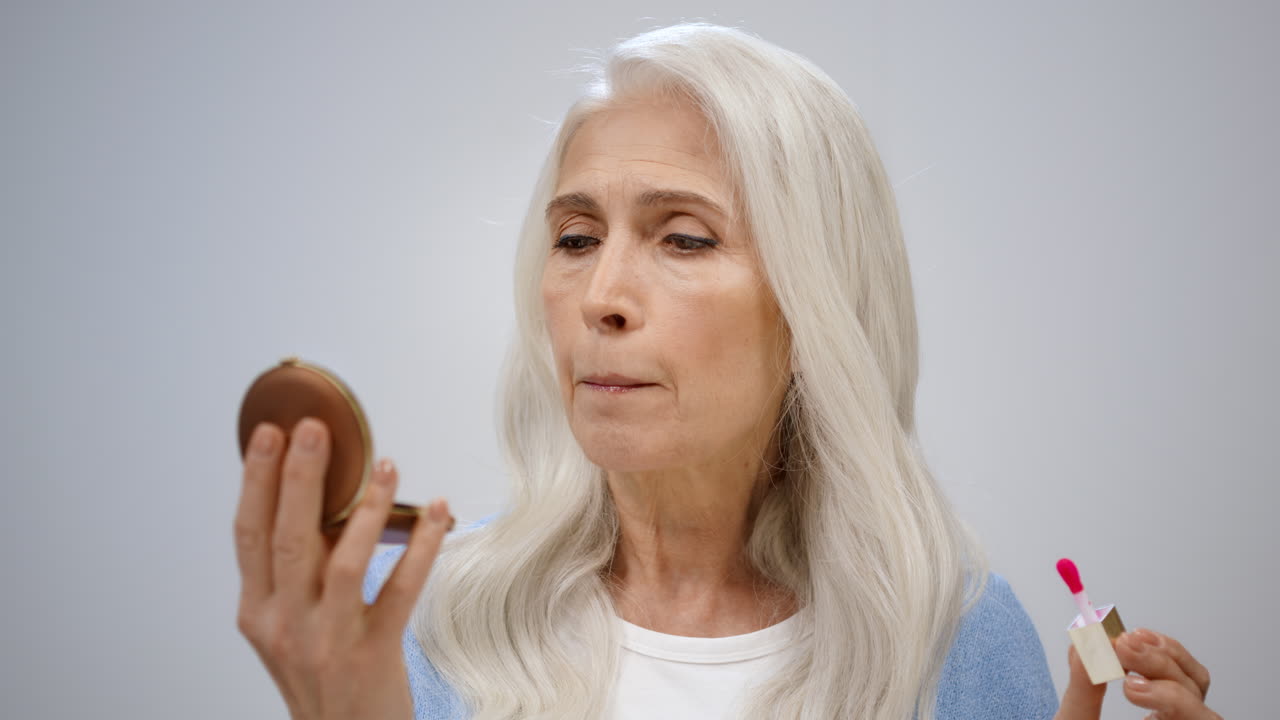 mujer mayor maquillándose en el estudio. mujer madura mirando el espejo en el interior.