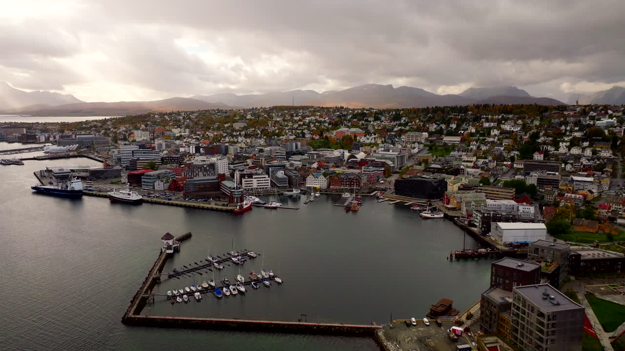 Drohnen-Kranfahrt über den Haupthafen und die Uferpromenade von Tromsø, Stadtbild Norwegens, dramatischer Himmel