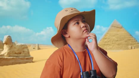 asian boy with a hat and binoculars thinking about something and looking around while traveling in giza pyramid. boy researcher, travel tourism adventure concept, close up