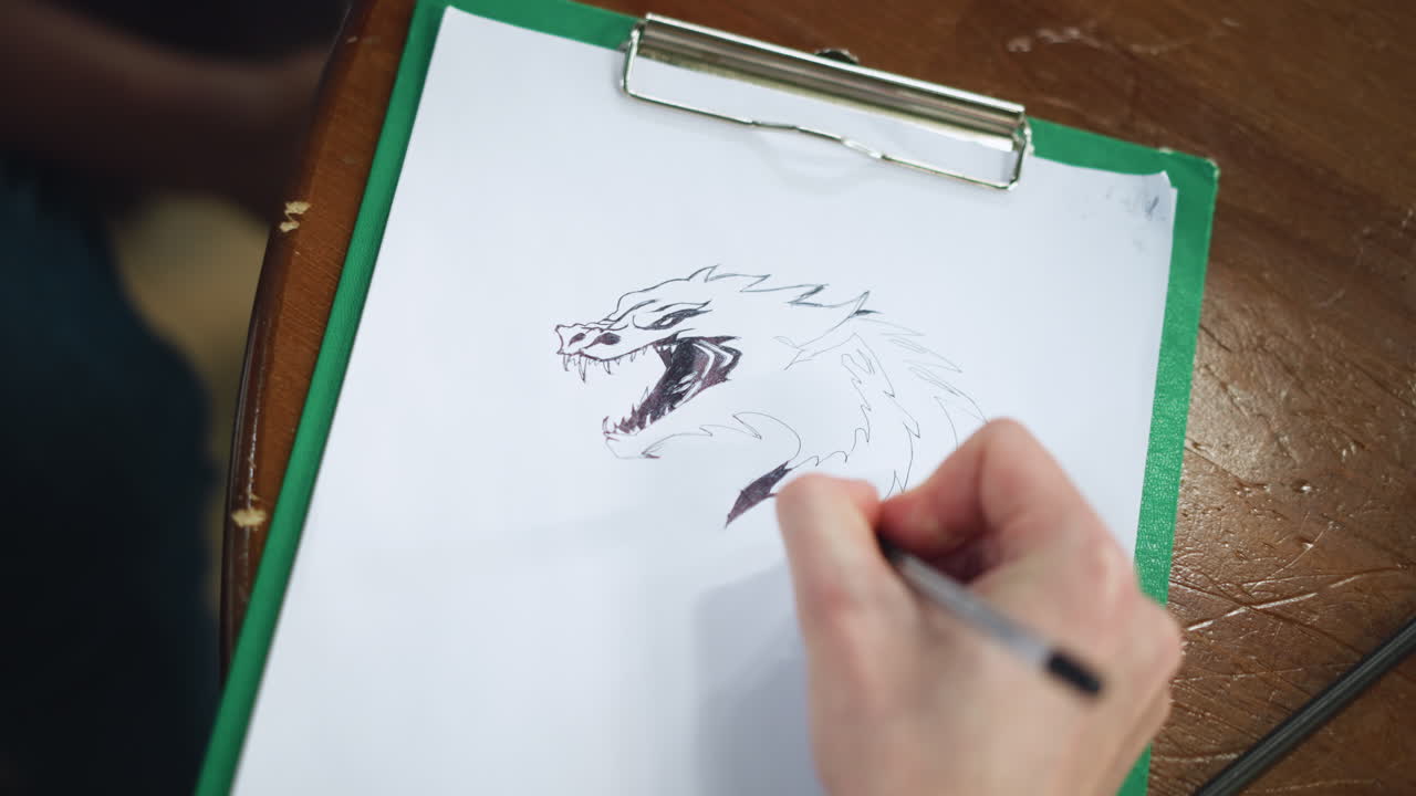 Head view of hand drawing detailed dragon head sketch on paper showing scales horns shading precise pen strokes capturing texture movement during focused creative process in real time with car