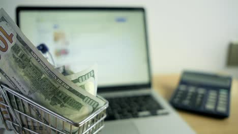 un primer plano de billetes de 100 dólares junto a una computadora portátil, una calculadora, números, un escritorio, un concepto de comercio electrónico, trabajo desde casa.