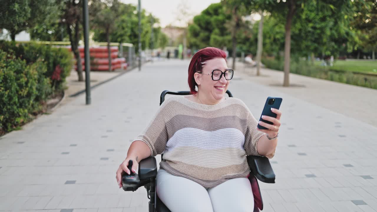Donna felice in carrozzina elettrica che usa lo smartphone al parco