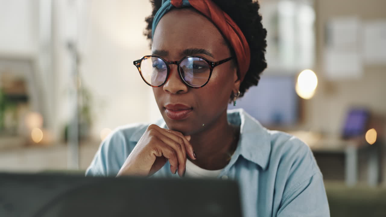 A woman with eyeglasses and headband working on a laptop