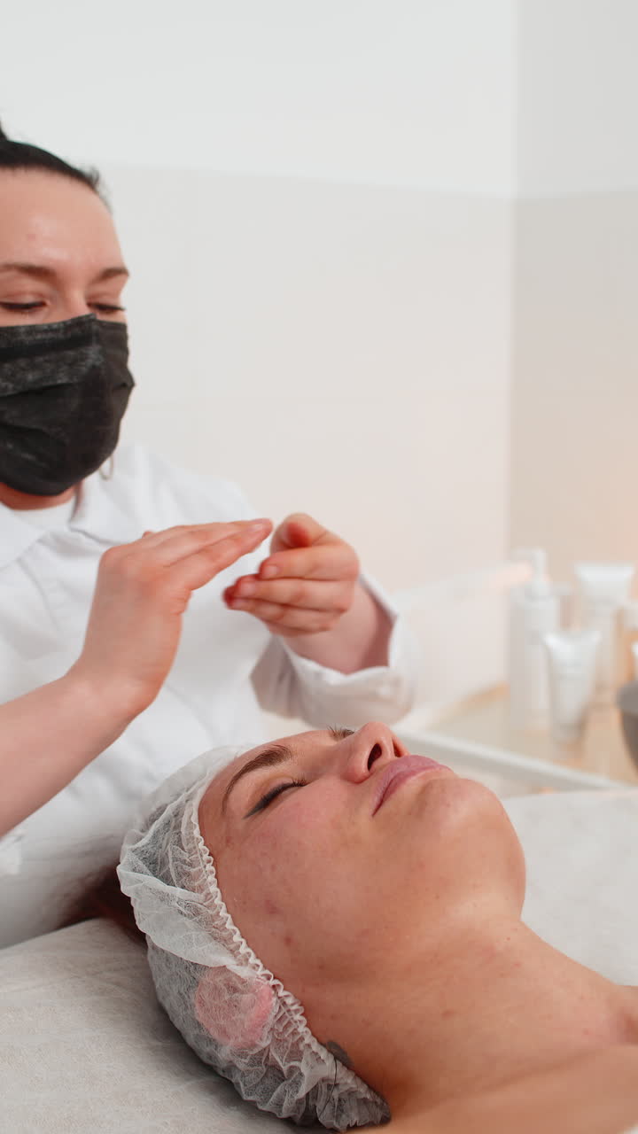 esteticista aplicando una máscara de crema hidratante química médica en el rostro de una mujer joven adulta