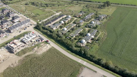 Aerial-overview-of-earthship-village-near-traditional-town---drone-pulling-back