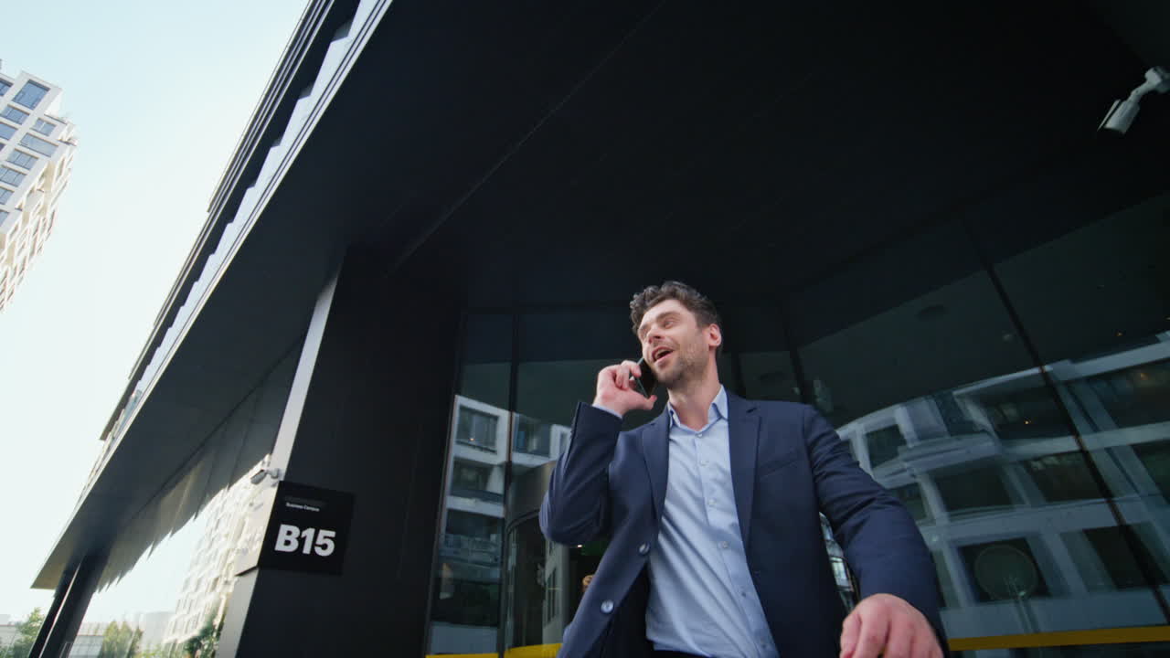 hombre de negocios satisfecho hablando por teléfono celular saliendo del edificio de la oficina. gerente feliz