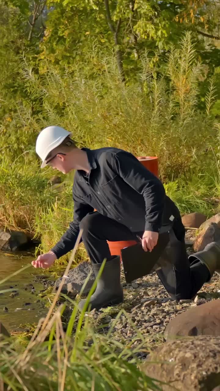 Vertical shot of technician kneeling by river writing notes after water check