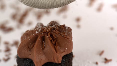 Icing-sugar-being-sieved-on-chocolate-cupcake