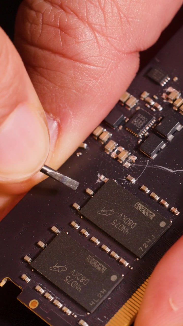 Macro shot of hands using a metal tool to inspect memory chips on computer hardware