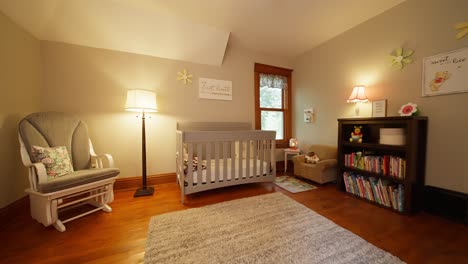 wide push in of a nursery with a grey baby crib, rocking chair, book shelf, and a lamp