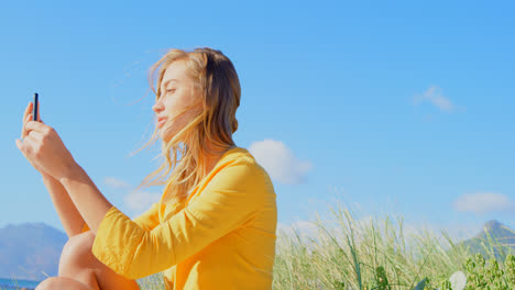 side view of young caucasian woman using mobile while sitting on the beach 4k