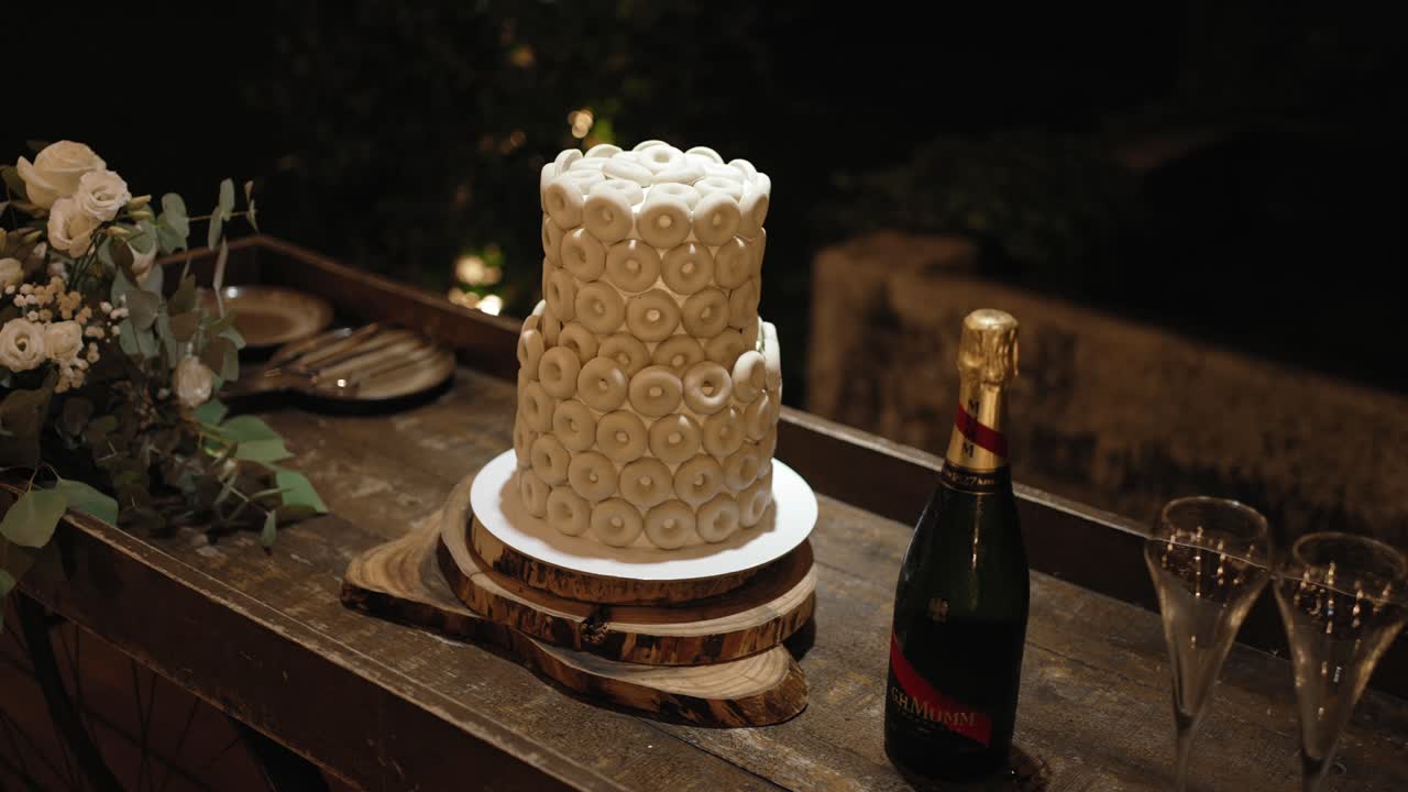 Elegant wedding cake covered in white cookies with champagne on a rustic table at night