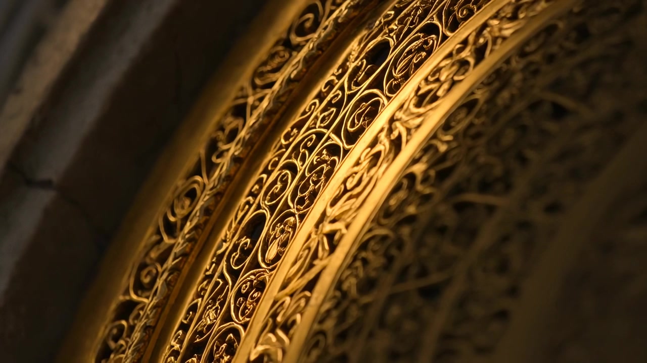 La telecamera si inclina rivelando una grata dorata all'interno di una cattedrale, mettendo in risalto la filigrana e lo stipite in pietra.