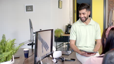 smiling man holding tablet, discussing robotic hand design with colleague in office