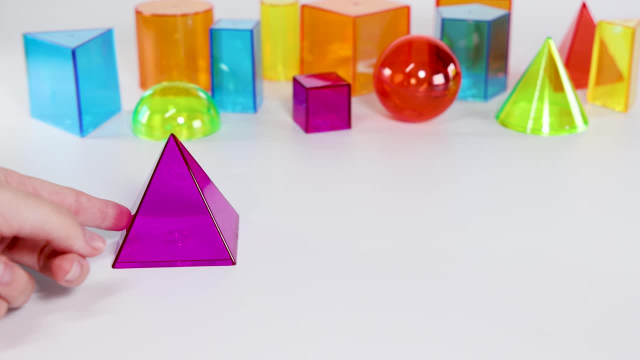 Hands interact with vibrant 3D geometric shapes on a white surface, highlighting educational concepts in a well-lit environment