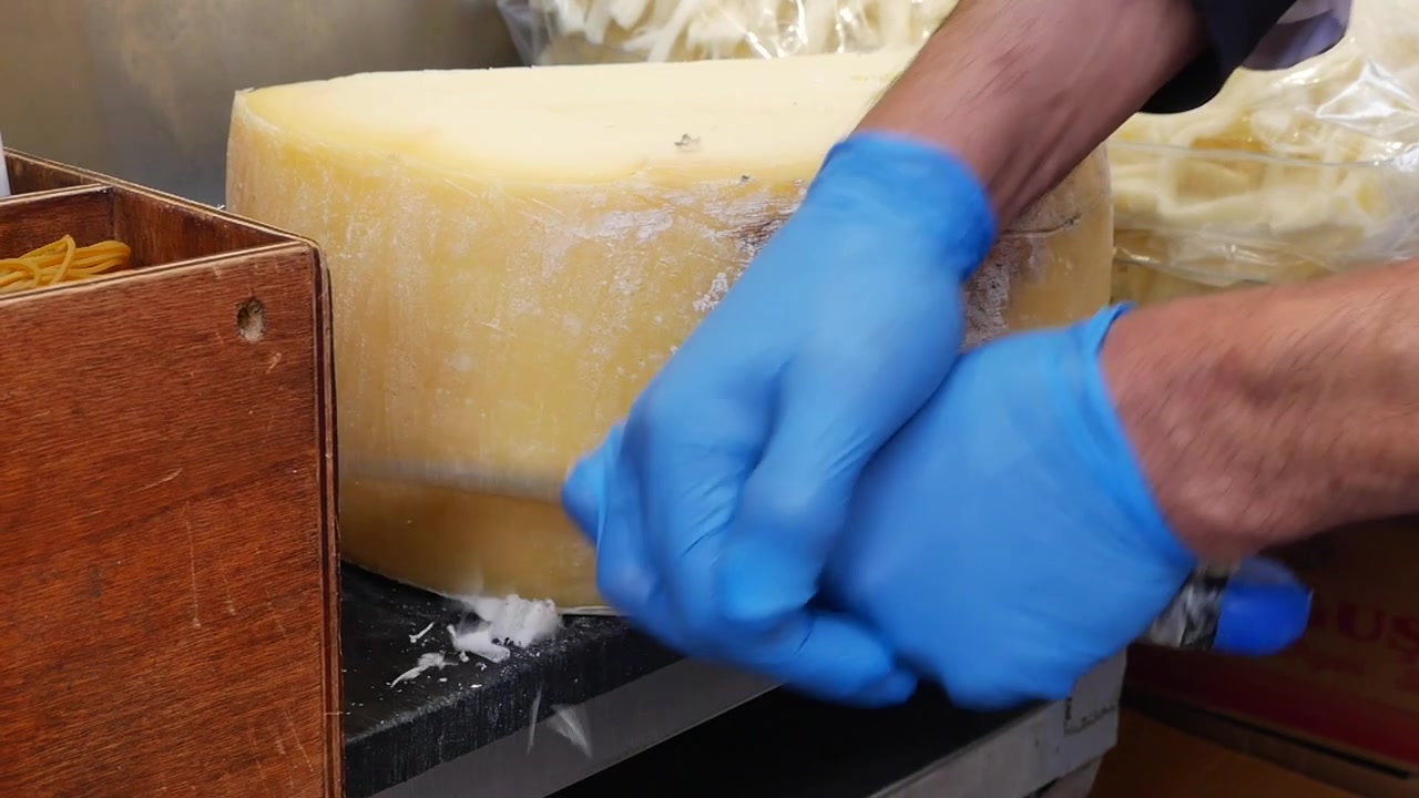 Gloved Hands Scraping Rind from a Large Cheese Wheel