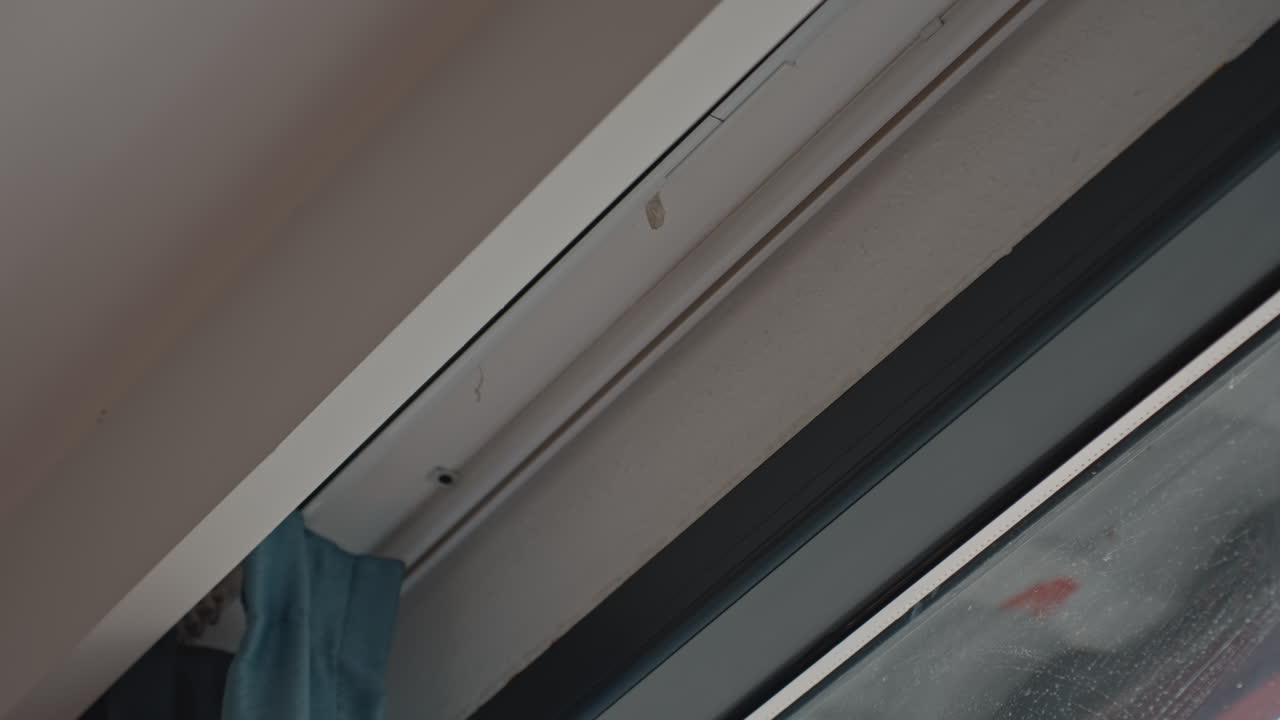 Dark torn curtain by rainstreaked window, closeup of blackout drape edge with small tear, wet glass pane and muted city lights outside, quiet gloomy atmosphere inside hotel room