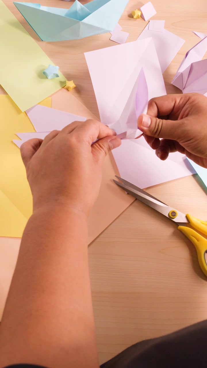 Overhead view of hands carefully folding purple paper into origami shapes on a wooden surface