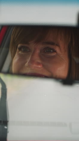 cheerful woman smiles driving car on empty road in city on rainy day. reflection of happy female driver with smile on face in mirror closeup slow motion