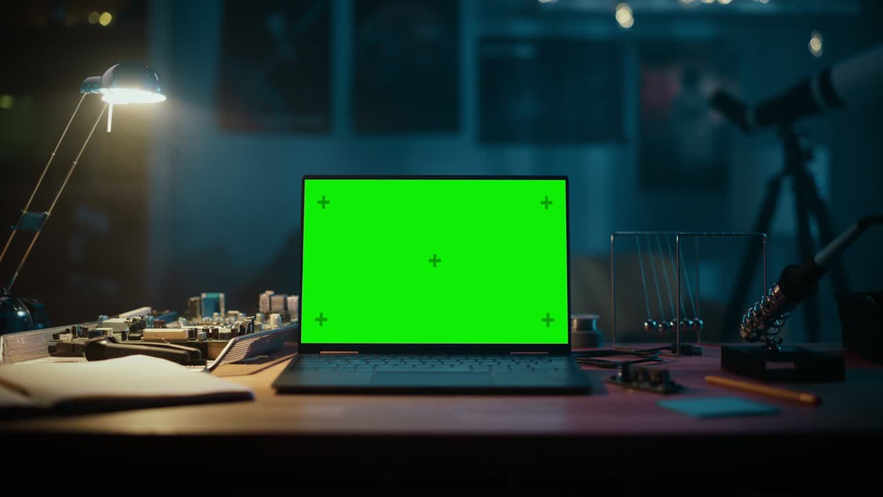Laptop Computer Standing on a Table with a Green Screen Chromakey Mock Up Display. Cozy Empty Room with a Lamp, Circuit Board, Newton's Cradle and Tools on the Table. Zoom In Footage.