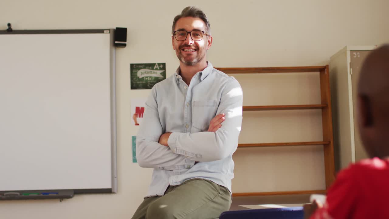 retrato de un feliz maestro caucásico sentado en un escritorio en el aula mirando a la cámara