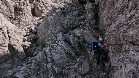 man climbs rocky mountain walls, dangerous passages with chains, summer, grignetta, and italian alps. aerial lateral drone
