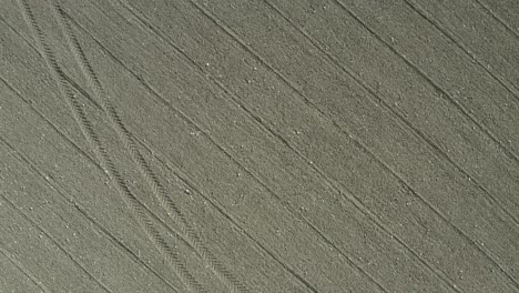 rising, rotating vertical aerial of rocky field reveals tractor tracks