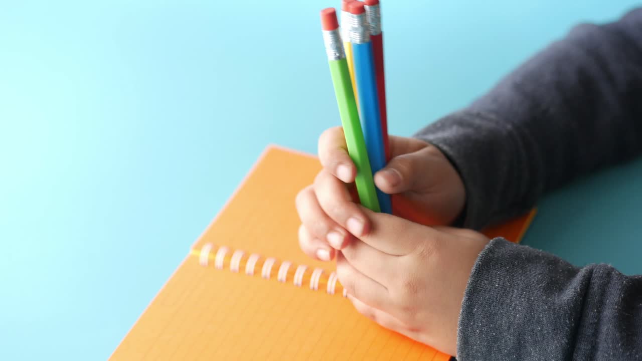 niño sosteniendo lápices de color sobre un cuaderno