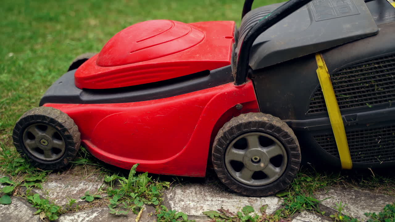 Trimming machine on grass. Red and black lawn mower cutting green grass near the stone path on the garden. Homeowner cleaning the yard. Close-up.
