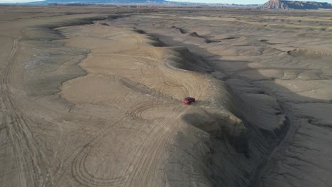 tracking drone shot of red van moving on hill and dirt road in dry desert landscape of utah usa