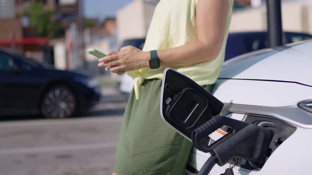 Woman using smartphone while charging electric vehicle