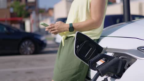 woman using smartphone while charging electric vehicle