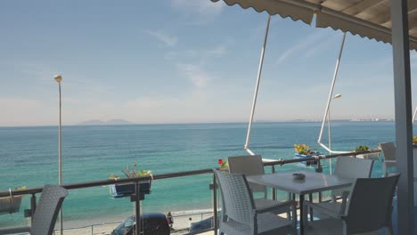 Forward-moving-shot-of-Albanian-Riviera-along-southwestern-coast-of-Albania,-from-an-empty-outdoor-cafe-balcony-on-a-sunny-day