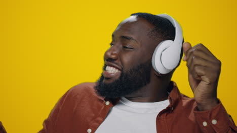 portrait of african guy enjoying music in headphones on yellow background.