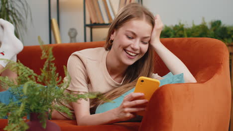 Young-woman-lying-on-sofa-at-home,-using-smartphone-share-messages-on-social-media-application