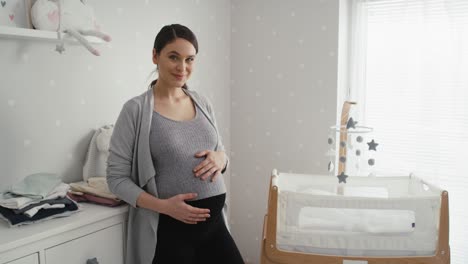 thoughtful caucasian woman in advanced pregnancy standing in the baby's room next to the crib.