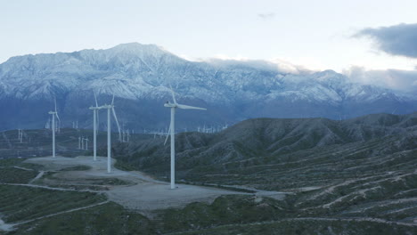 Luftaufnahme-Von-Windkraftanlagen-Mit-Einem-Großen-Schneebedeckten-Berg-Dahinter