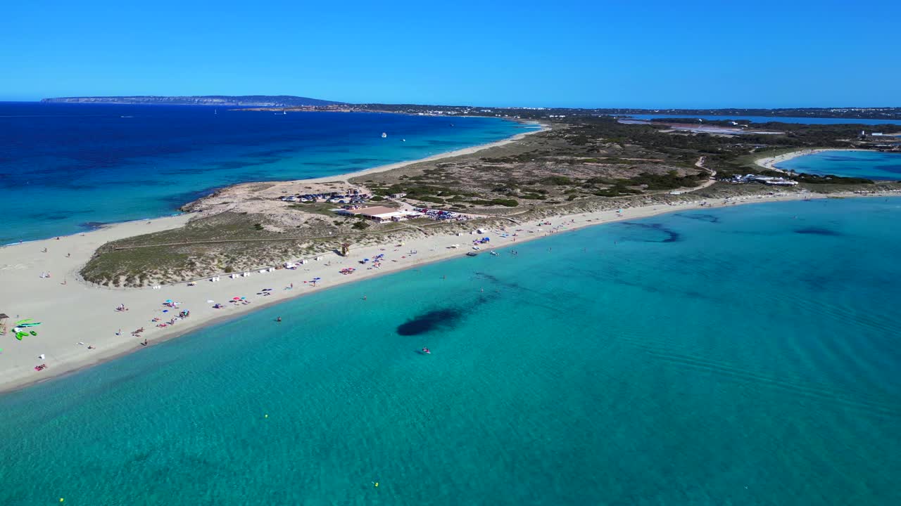 Platja de Ses Illetes beach on formentera with clear turquoise Blue ocean and people relaxing under a clear sky. Nice aerial view panorama overview static tripod hovering drone