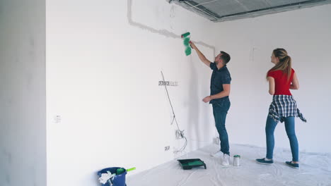 Una-Mujer-Besa-A-Un-Hombre-Con-Camisa-Azul-Pintando-Una-Pared-Blanca-En-La-Habitación