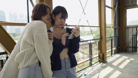 two young women looking at a smartphone in an urban industrial setting