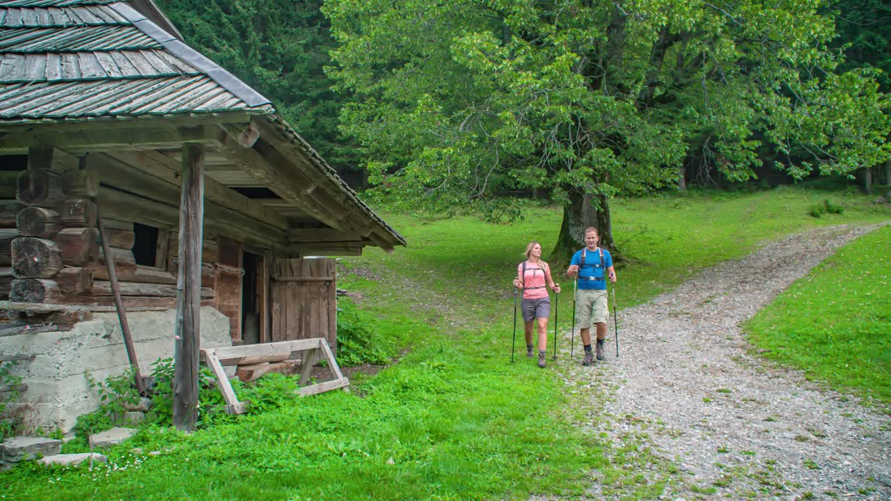 Young couple walking with hiking sticks down a dirt road alongside building