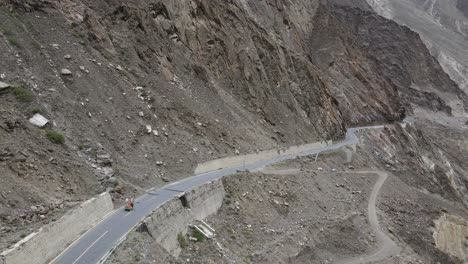 Vista-Aérea-Del-Vehículo-Rickshaw-Moviéndose-En-La-Carretera-En-Las-Tierras-Altas-De-Pakistán,-Rastreando-Disparos-De-Drones