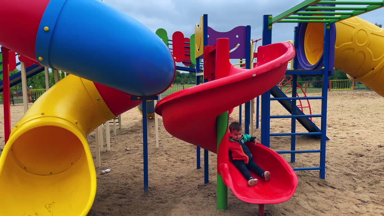 Caucasian toddler sliding down on the playground. Child spending time outdoors.