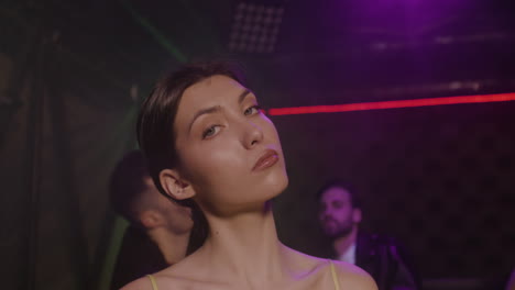 retrato de una hermosa chica mirando con confianza a la cámara en la discoteca mientras sus amigos bailan detrás de ella 2 1