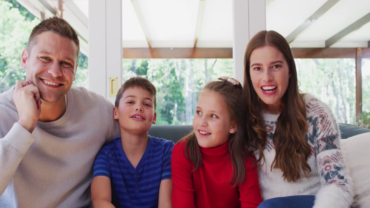 카우카시안 가족의 초상화 웃고 카메라를 흔들며 소파에 앉아 있습니다.