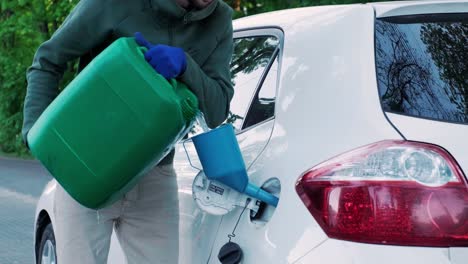 a man pouring gasoline into an empty fuel tank from a plastic red gas can. filling the car from the canister into the neck of the fuel tank.