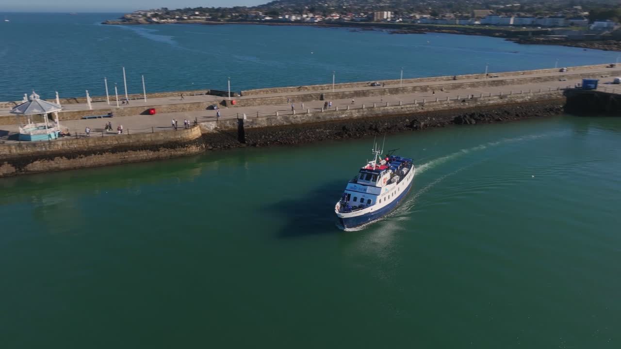 Dublin Bay Cruises Boat, Dún Laoghaire, County Dublin, Ireland, September 2024. Drone follows and orbits the ferry with shimmering sparkling reflections in the water as onlookers watch from East Pier.